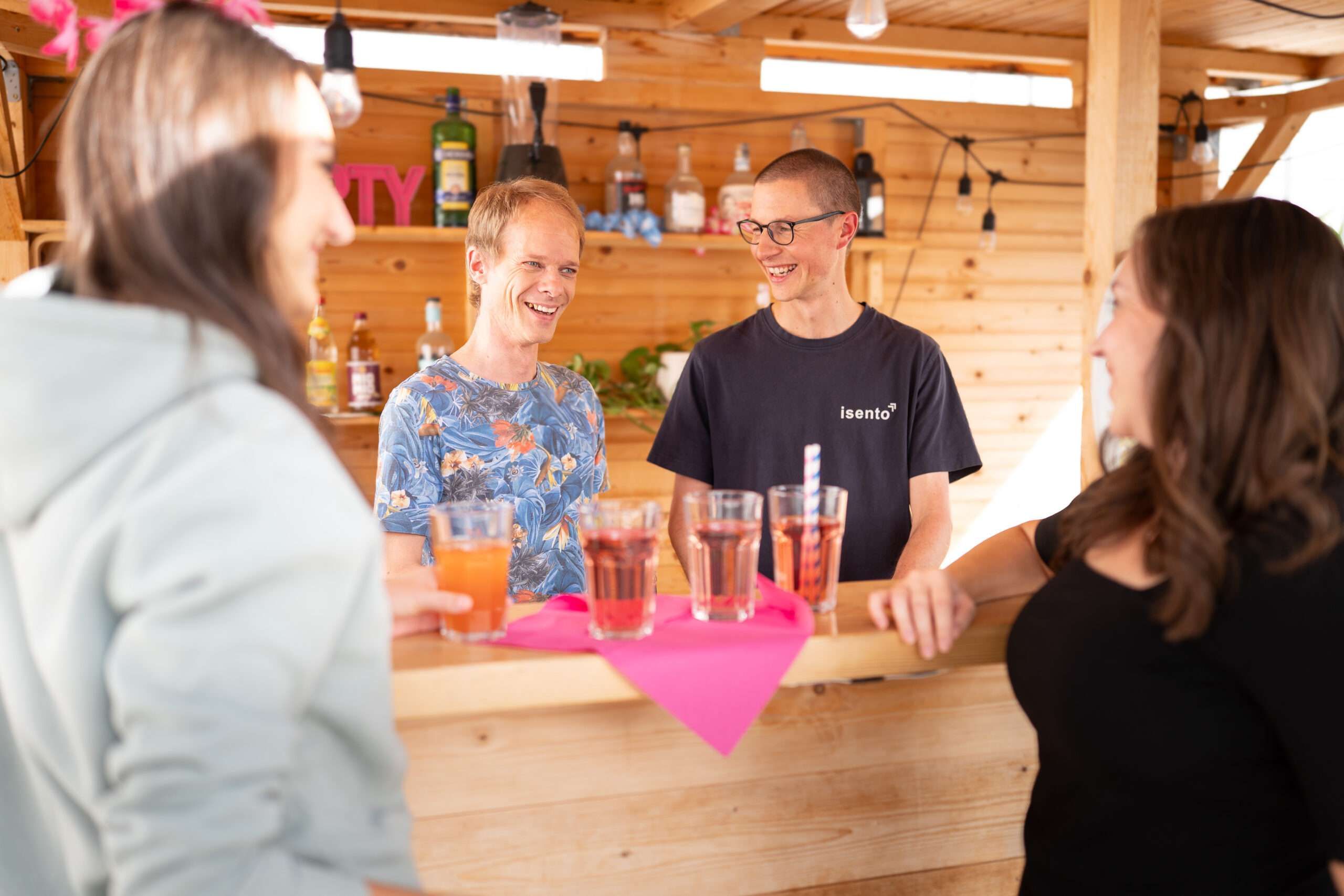 Mitarbeitende lachen an einer Holzbar bei einem Sommerfest