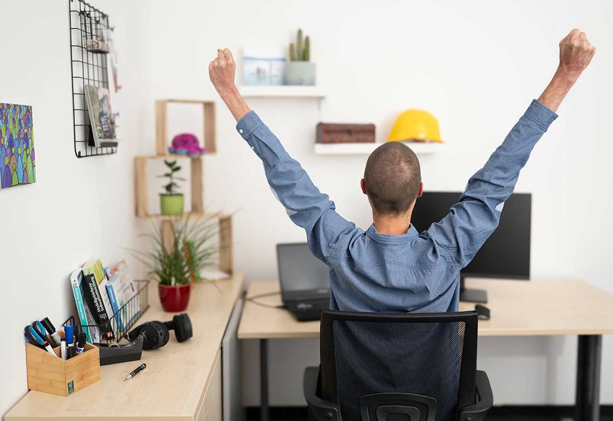 Eine Person von hinten an einem Arbeitsplatz mit in die Höhe gereckten Händen