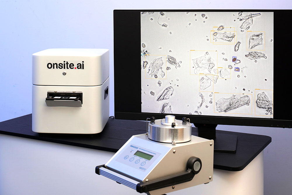 Das onsite.ai-Messgerät PartSens neben einem Monitor mit mikroskopischer Aufnahme von Luftpartikeln und einem Luftprobensammler